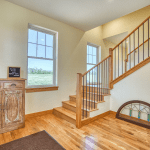 Wood staircase with wooden steps and black metal balusters rises beside a large windowed wall; antique carved cabinet and a leaning stained-glass panel on the floor nearby.