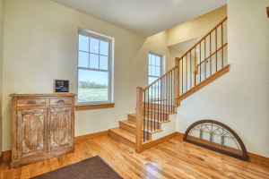 Wood staircase with wooden steps and black metal balusters rises beside a large windowed wall; antique carved cabinet and a leaning stained-glass panel on the floor nearby.