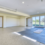 Bright, empty garage or showroom with white walls, wide glass doors to the outdoors, and rubber floor mats along the entry area