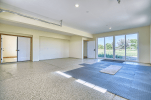 Bright, empty garage or showroom with white walls, wide glass doors to the outdoors, and rubber floor mats along the entry area