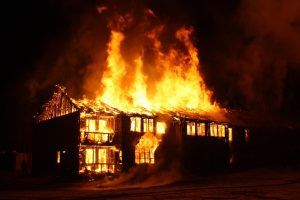 Two-story wooden house fully engulfed in flames at night with glowing windows
