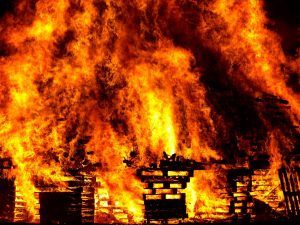 Massive blaze engulfing stacked wooden pallets, bright orange flames filling the scene at night