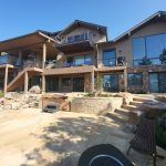 Exterior of a contemporary multi‑level house with large glass windows, stone facade, and wooden decks.