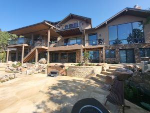 Exterior of a contemporary multi‑level house with large glass windows, stone facade, and wooden decks.