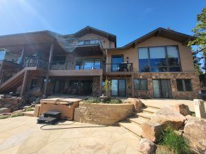 Modern two-story house with stone base, large windows, and multiple balconies under a clear blue sky.