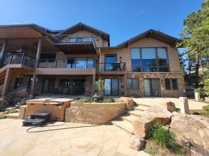 Modern two-story house exterior with a stone foundation, large windows, and a wooden deck under a clear blue sky.