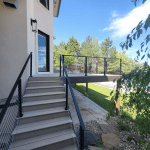 Outdoor staircase along a modern home with metal cable railings, leading to a deck with a patio table under a blue sky.