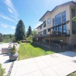 Modern two-story house with expansive glass windows and a balcony overlooking a manicured backyard on a sunny day.