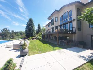 Modern two-story house with expansive glass windows and a balcony overlooking a manicured backyard on a sunny day.
