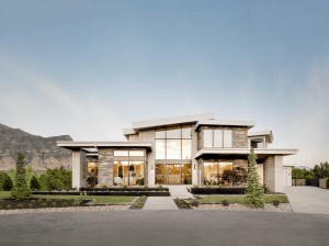 Modern two-story house with stone and glass facade, landscaped front yard, and distant mountains under a blue sky.