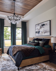 Bedroom with a wooden plank ceiling chandelier above a dark bed, green curtains, and abstract wall art framed on the right side.