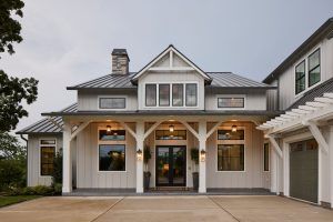 Modern farmhouse facade with gray siding, gabled dormer, and lit lanterns at the front entry.