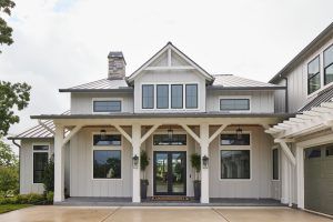 Front view of a modern gray house with a stone chimney, large windows, and a covered entryway.