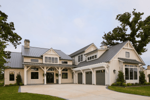 Front view of a beige, multi-garage suburban home with a gray metal roof and white trim under a clear sky.