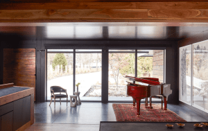 Red grand piano on a Persian rug in a modern room with dark wood walls and large glass doors to the outdoors