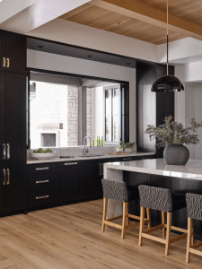 Modern kitchen with dark cabinetry, marble countertops, and a marble-topped island with two patterned bar stools.