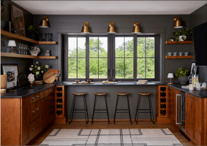 Contemporary kitchen with dark gray walls, a large window, and five metal bar stools at a wooden counter.